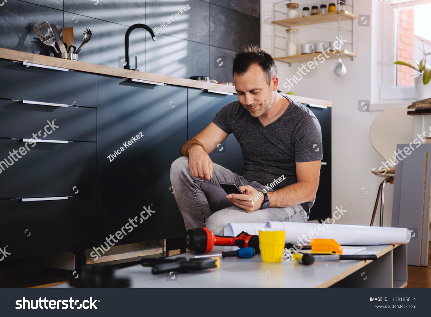 stock-photo-man-working-on-a-new-kitchen-installation-and-using-a-smart-phone-1139185814